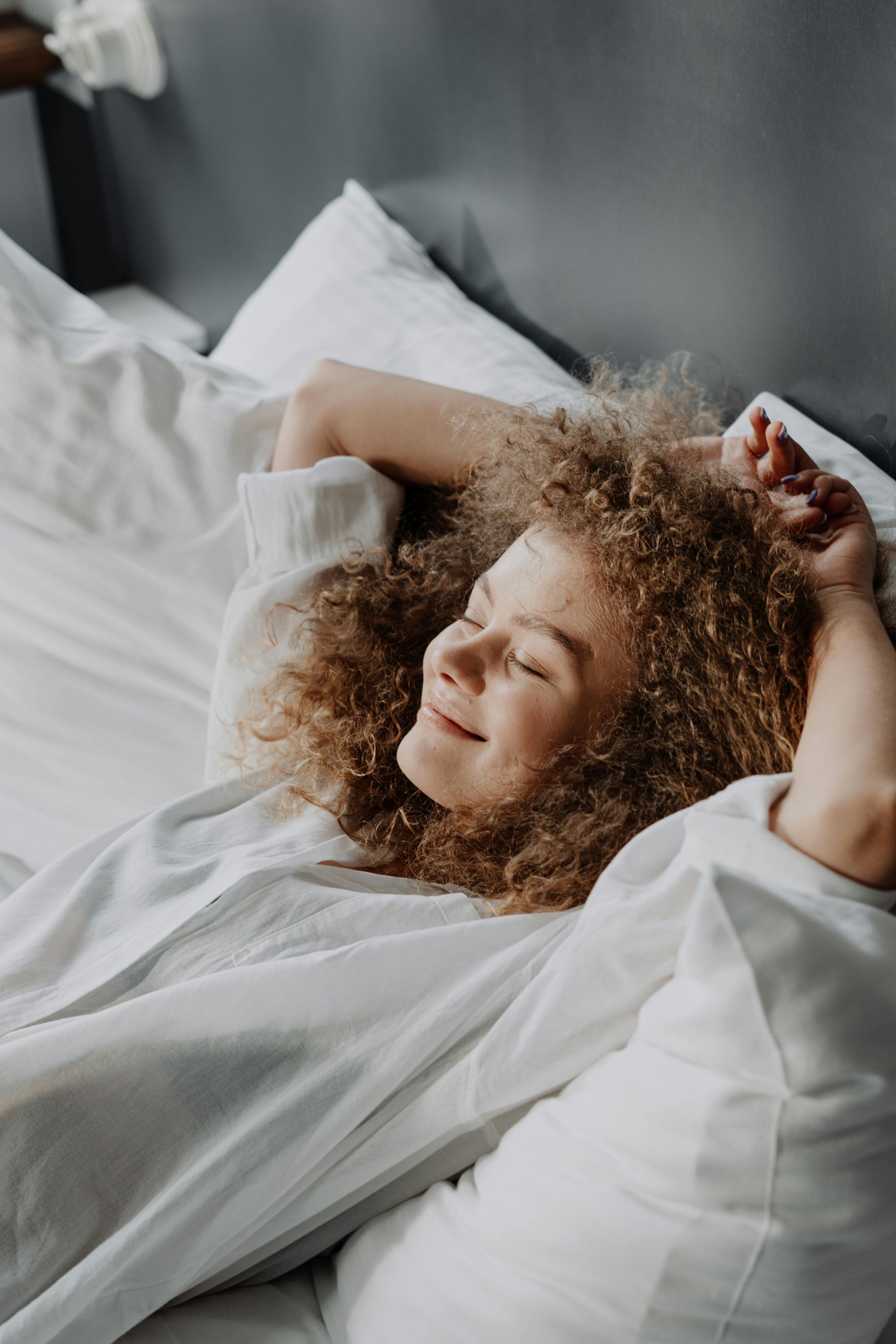 A woman rests with her eyes closed and a smile on her face, her arms behind her head, enjoying the sunset reflected upon her.