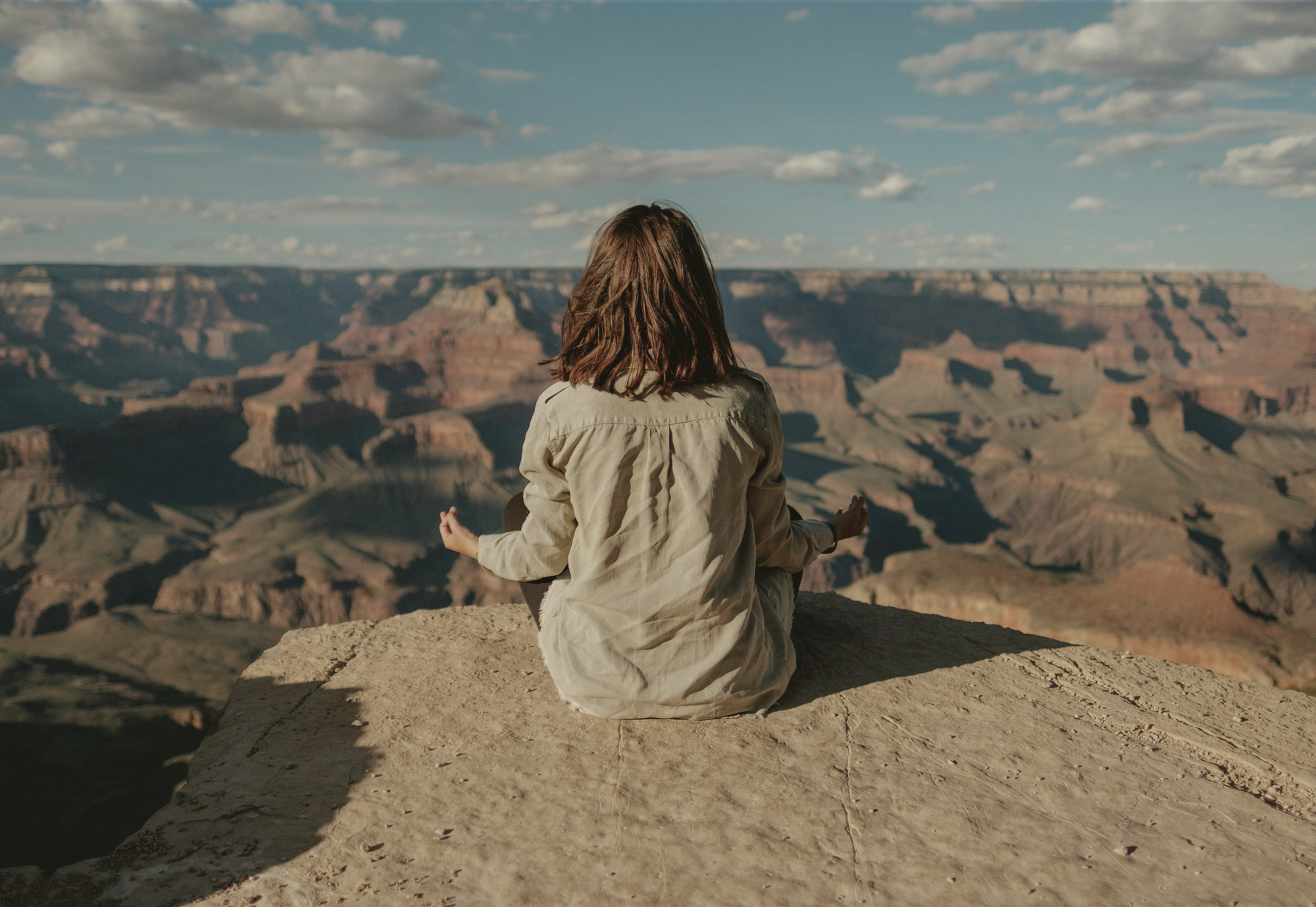 Woman meditating on a rock ledge overlooking the Grand Canyon.